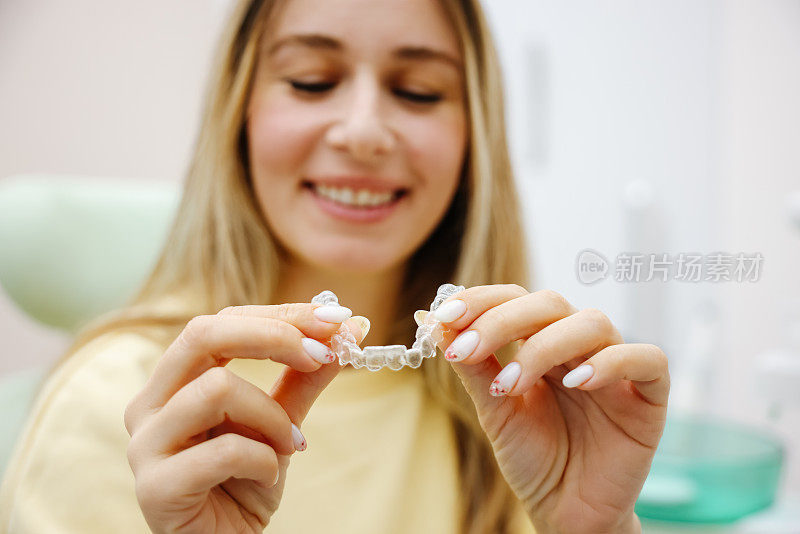 牙科隐形牙套或硅胶训练器在一个年轻的微笑女子的手中。正畸概念- Invisalign